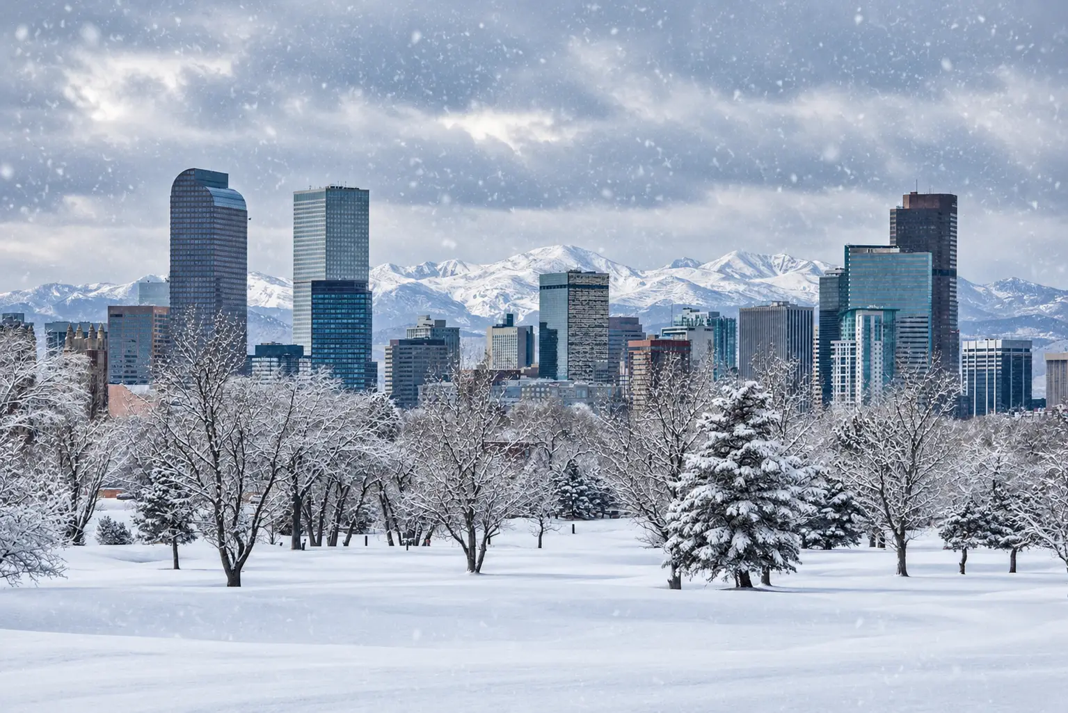 Commercial snowplow clearing a snow-covered roadway with Denver in the background